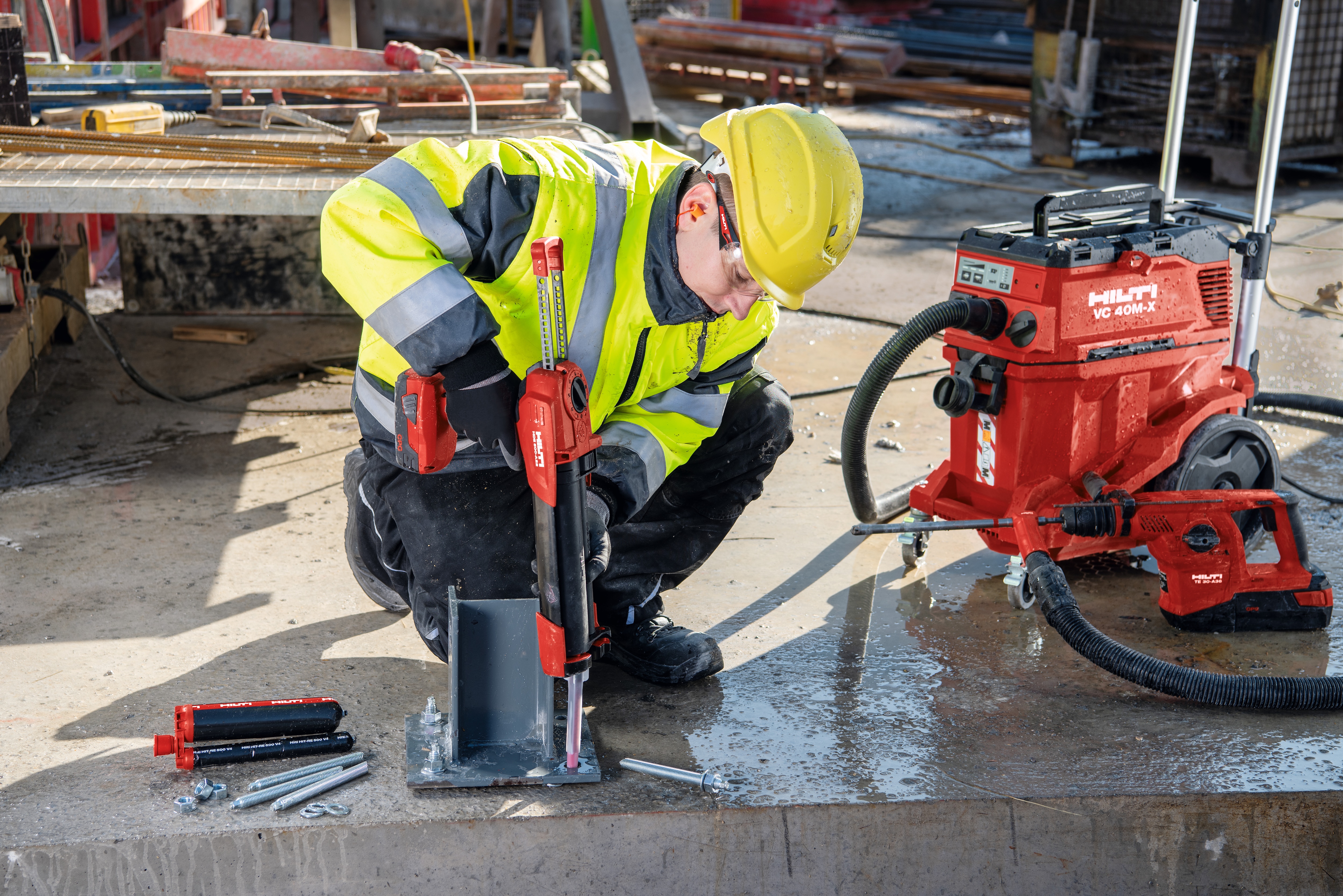 Construction worker in yellow high visibility vest injecting chemical anchor into a drill hole in concrete.