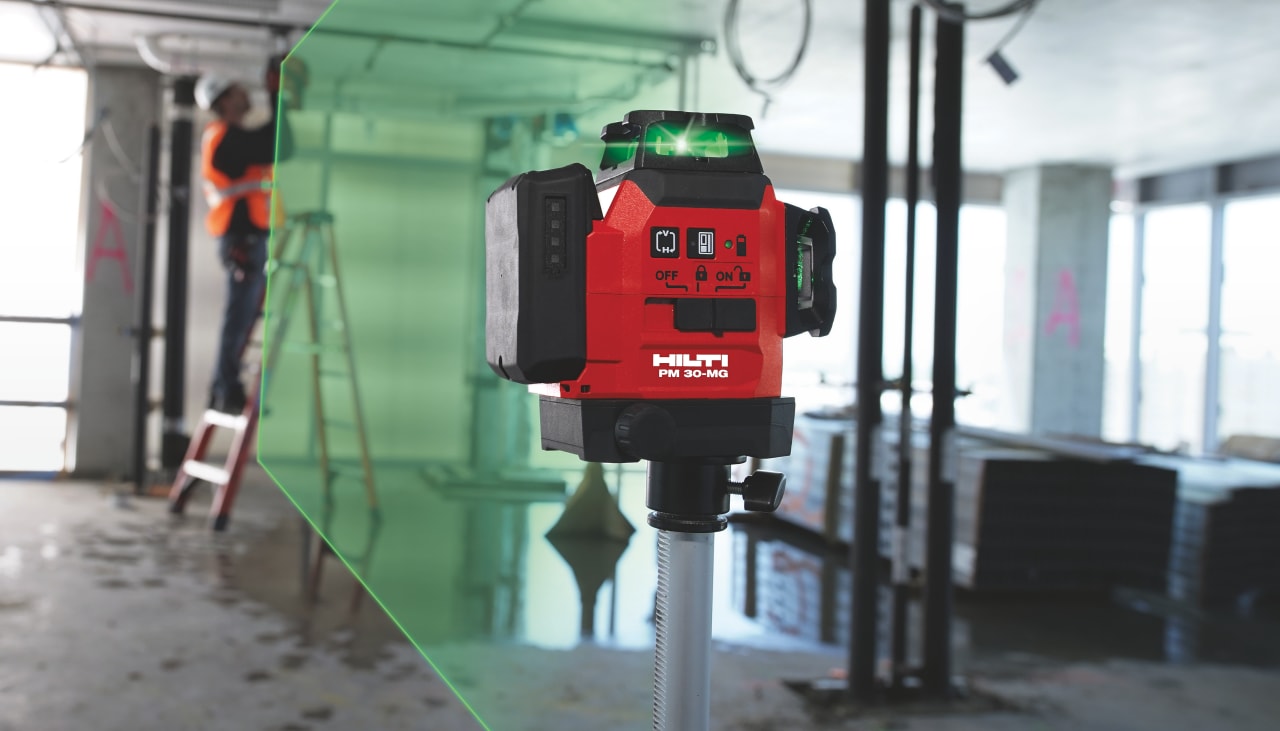Hilti red laser PM - 30 MG meassuring with green light and in the background construction worker drilling a hole in the line of the laser.