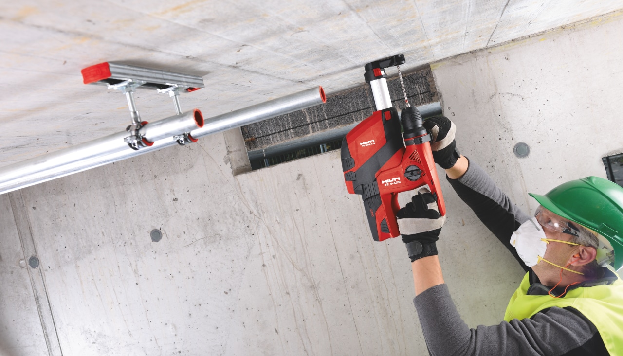 Construction worker in yellow high visibility vest is drilling a hole to concrete sealing with red Hilti Hammer drill with dust attached dust extractor.