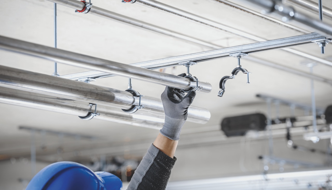 Close up of a man connecting pipe into modular support system at ceiling.