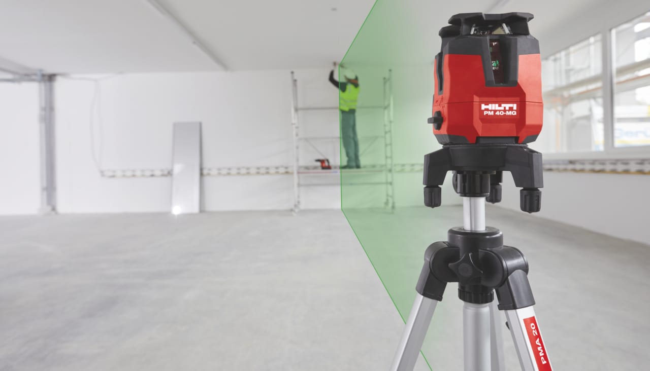 Close up of red Hilti laser showing a green lane where construction worker in yellow high visibility vest drilling a hole in the ceiling.