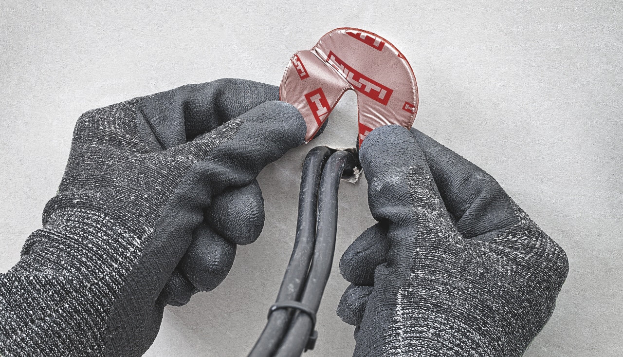 Close up of hands in safety gloves installing Hilti firestop solution around cables.