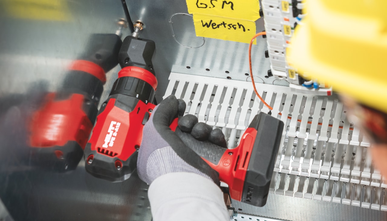Construction worker in yellow helmet using Hilti red drill driver inside of a stainless steel box.