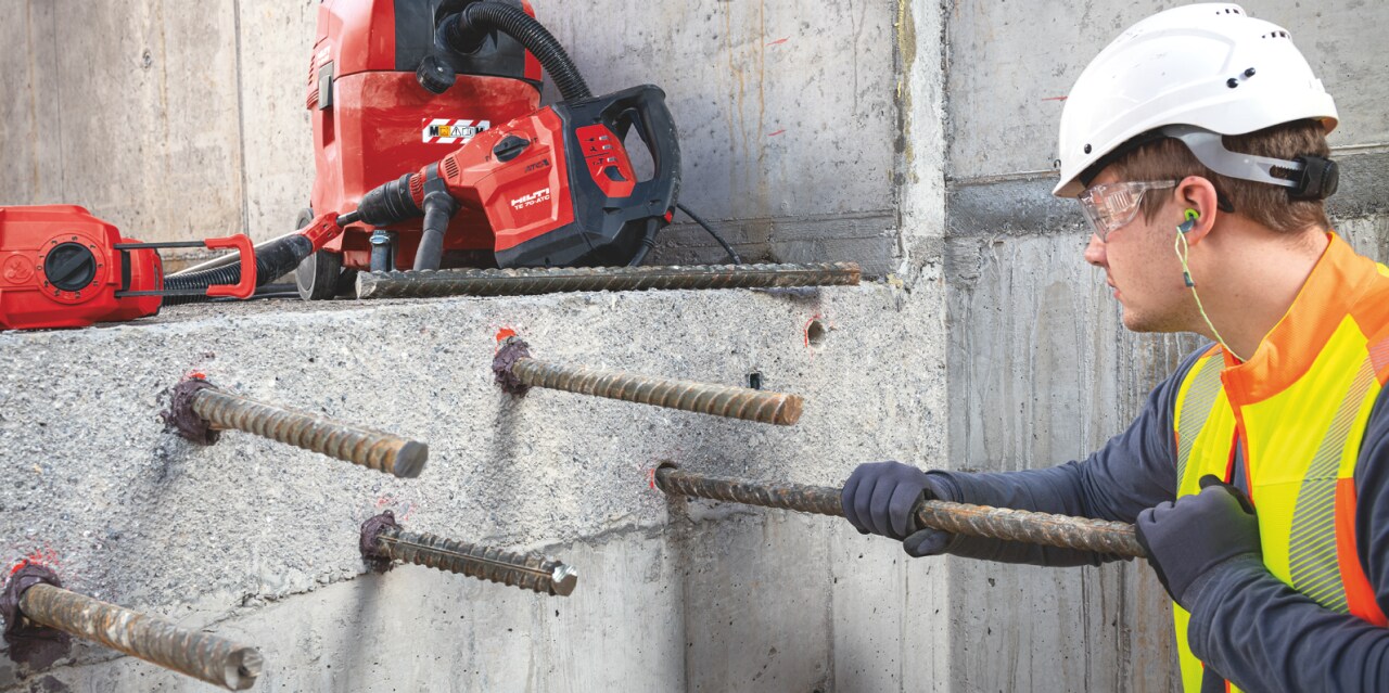 Construction worker in yellow high visibility vest and blue helmet using Hilti red direct fastening tool for the ceiling.Construction worker in yellow high visibility vest working on installation of metal anchor into a concrete wall.