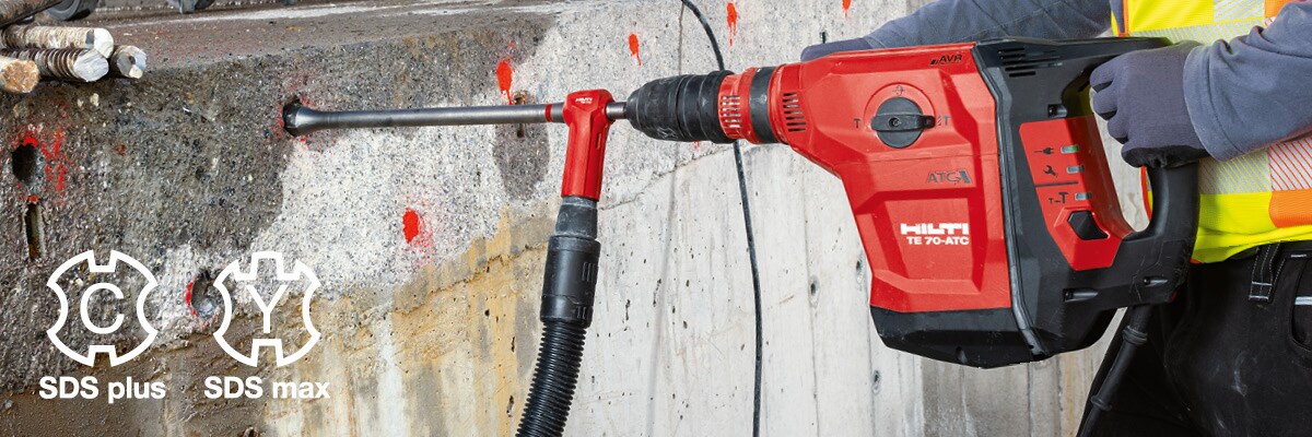 Man in yellow high vis vest drilling a hole into the concrete with Hilti Red Hammer Drill.