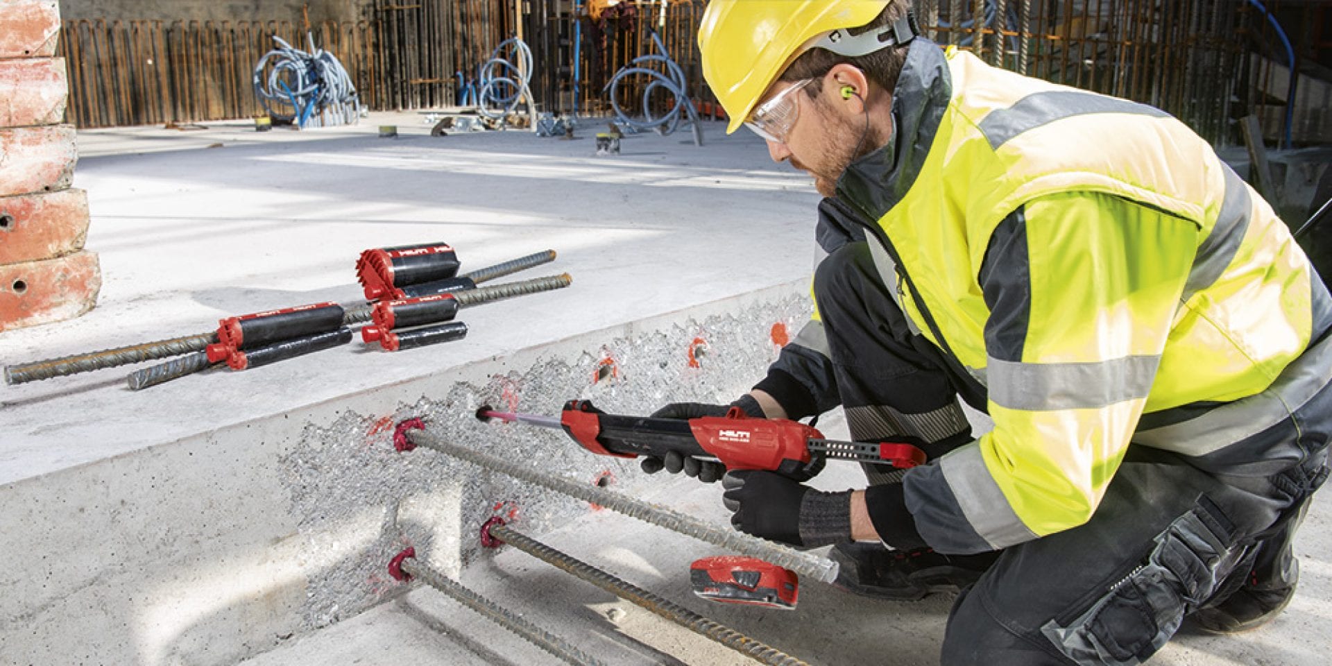 Man in yellow high vis vest injecting chemical anchor into the concrete with Hilti Red injection mortar. 