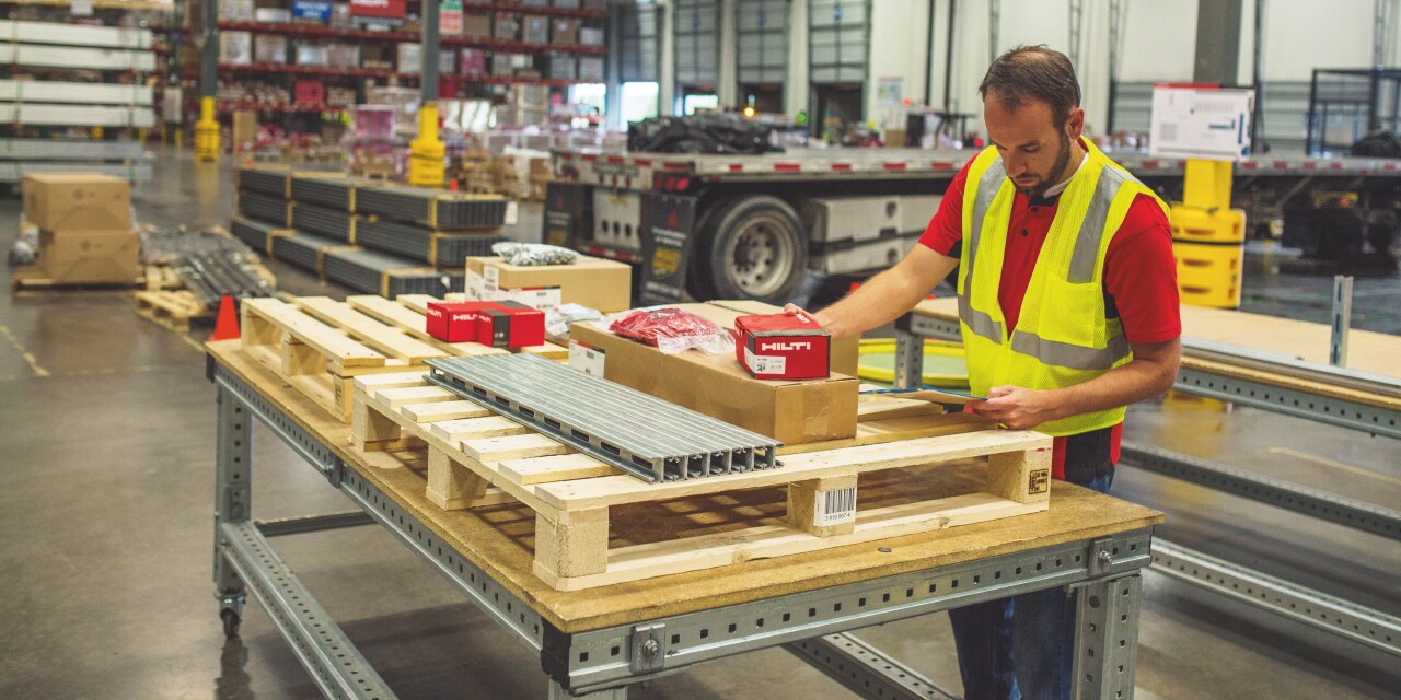 Man in yellow high visibility vest organizing red Hilti boxes on pallet.