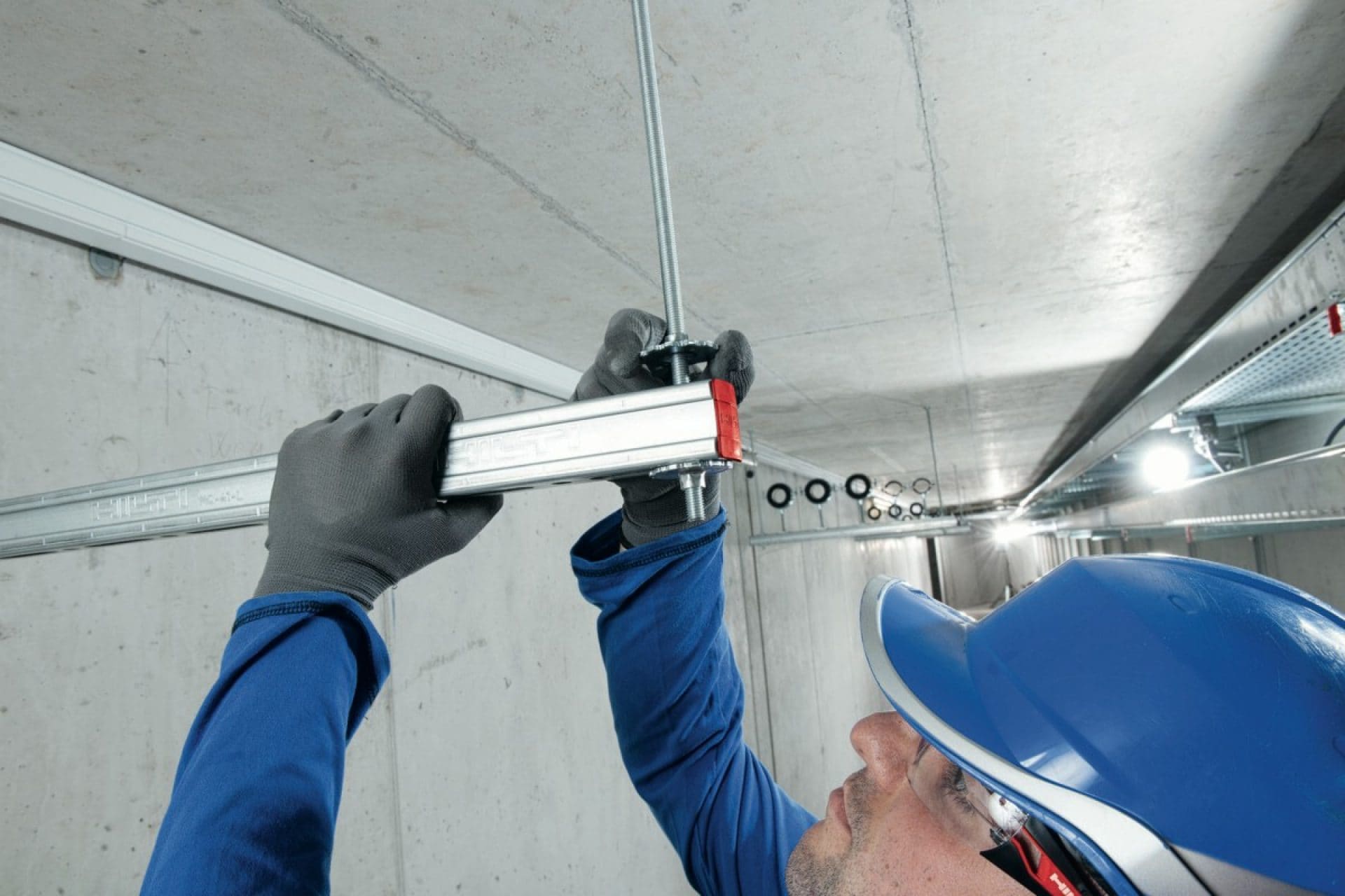 Construction worker installing Hilti modular system for piping and cables to ceiling.