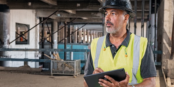 A construction worker wearing high visibility vest and having tablet in hand