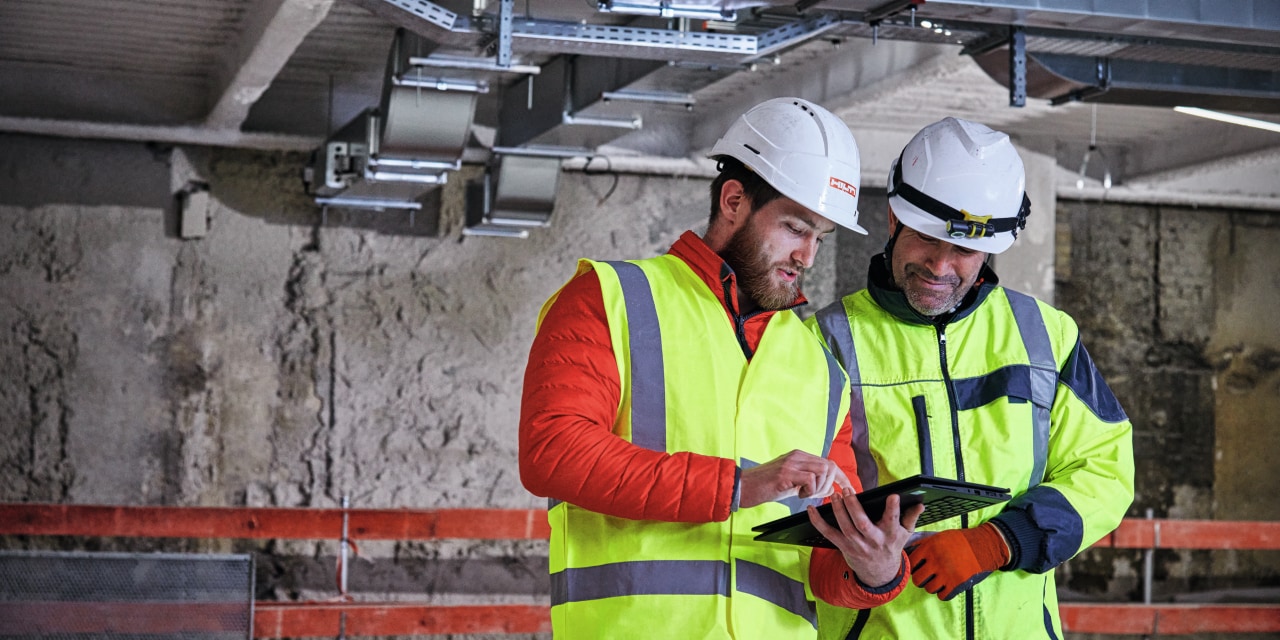 Hilti Account manager talking to a customer. Both wearing yellow high visibility vests and helmets. 