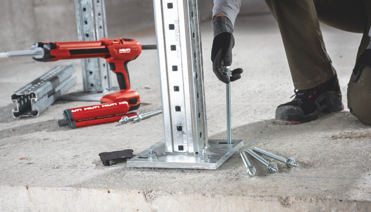 Worker is installing mechanical rebar to the concrete floor, to fix support construction. Next to him is red Hilti chemical anchor dispenser.