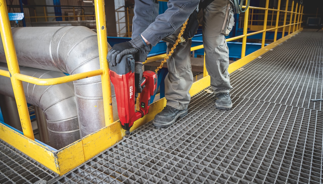 Construction worker is using Hilti Red direct fastening tool in a metal construction floor in a factory hall.