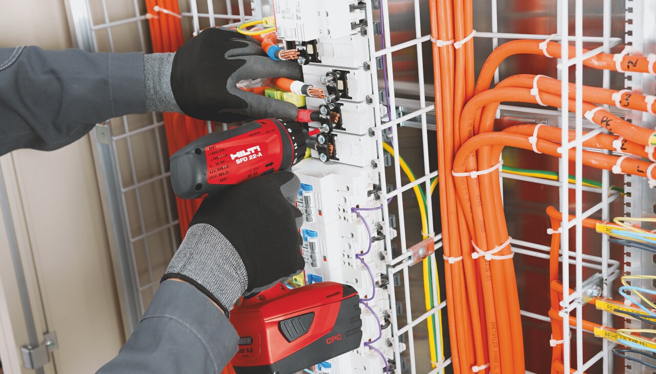 Man is using red Hilti screw driver and installing wires and screws into a fuse box.