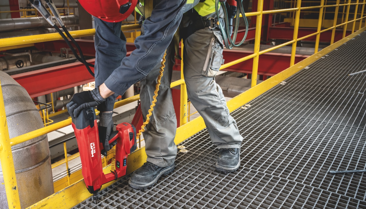 Construction worker using Hilti Red direct fastening tool on a metal construction floor.