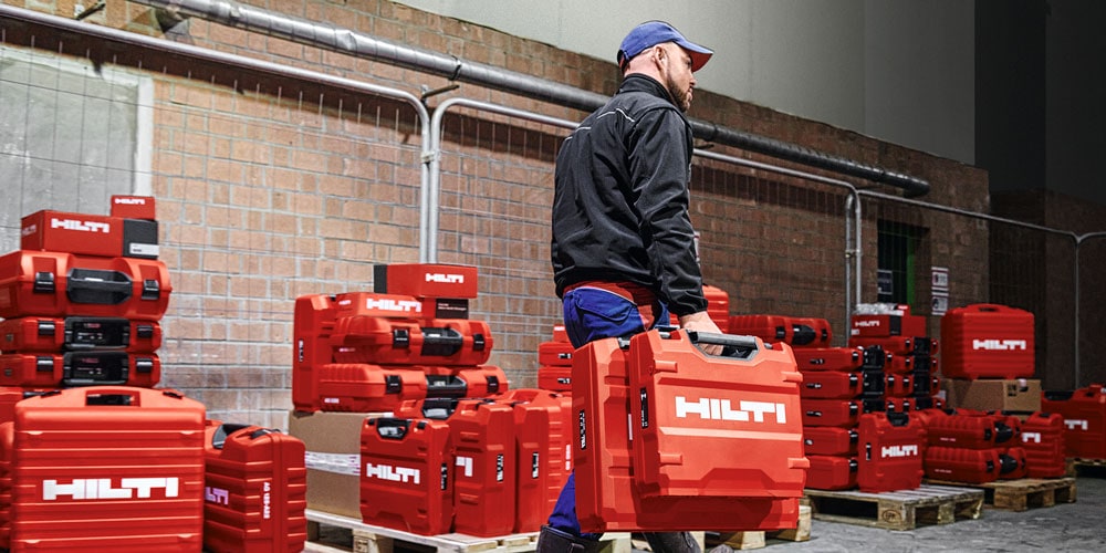Man walking with Hilti red tool box next to pallets with tool boxes.