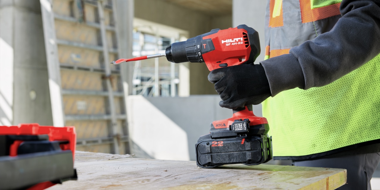 Construction worker in yellow high visibility vest holding Hilti red screw driver in hand. 