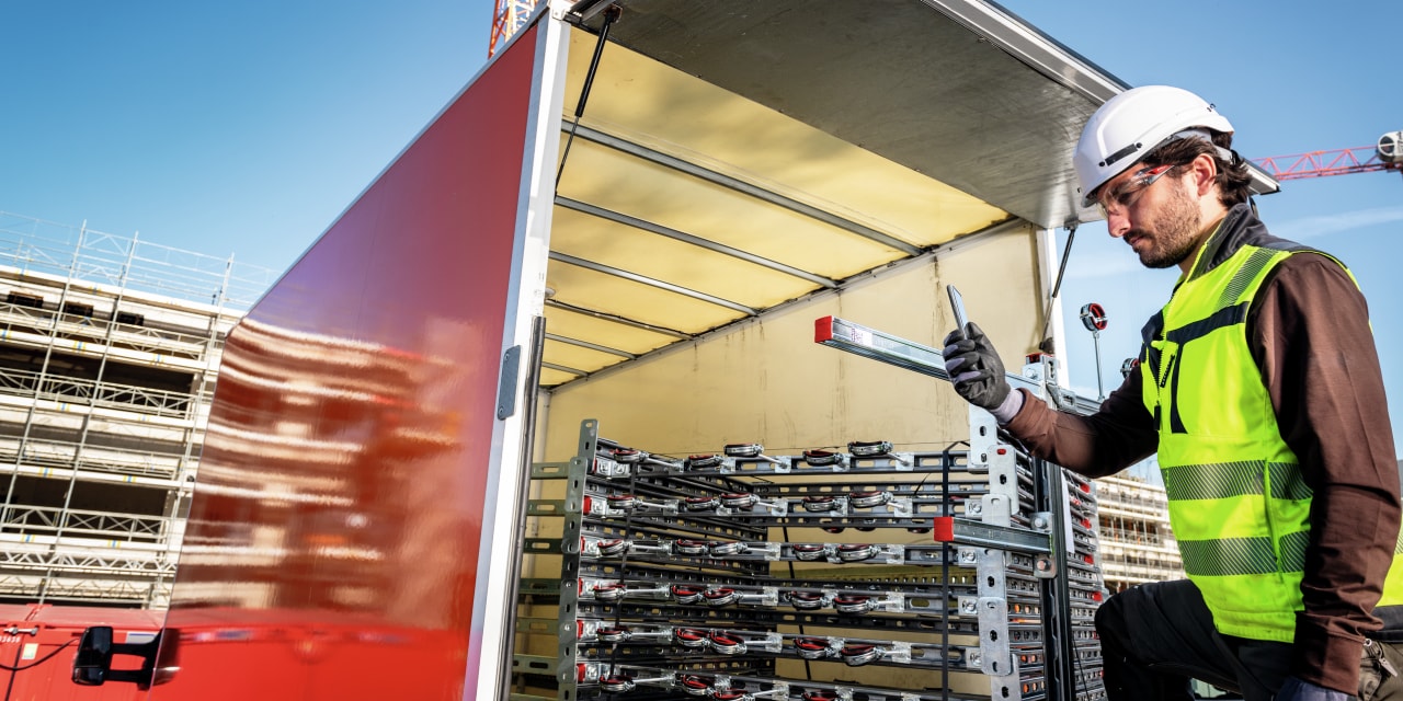 Construction worker in yellow vest is unloading van full of Hilti modular support systems. 