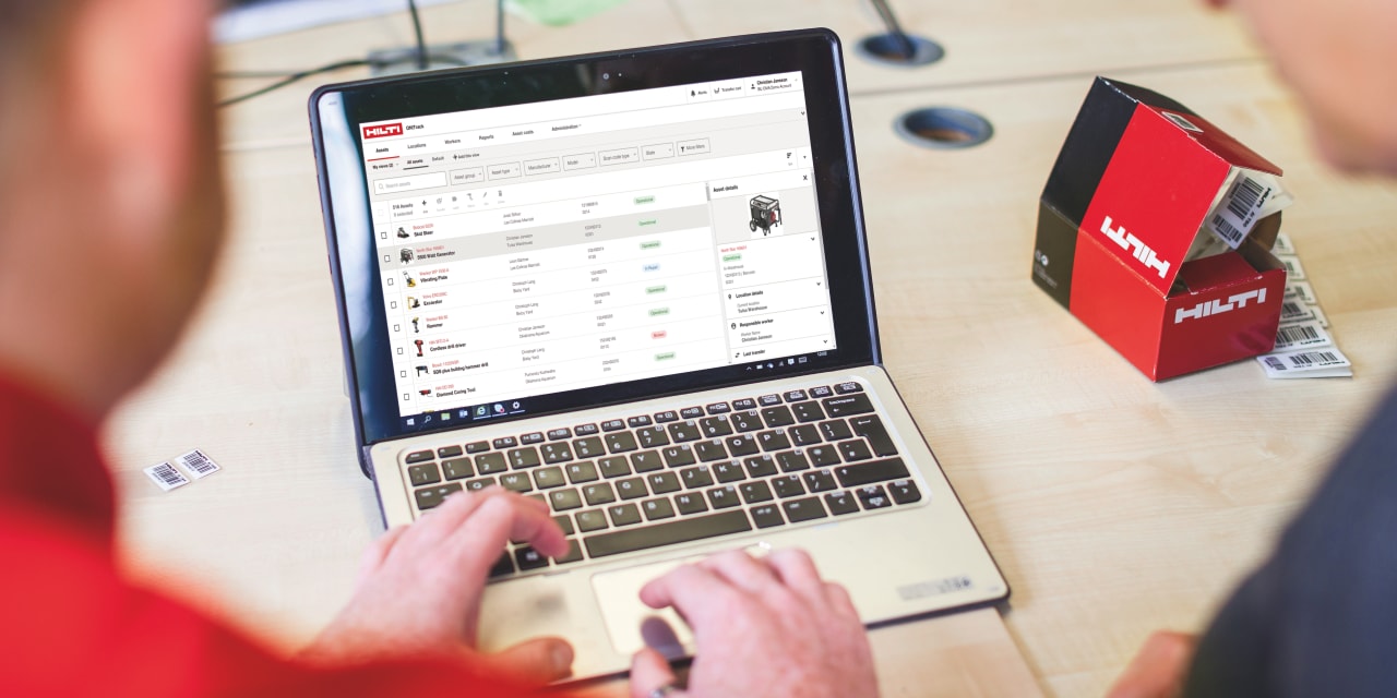 Two men using laptop, on the screen is asset management software. 