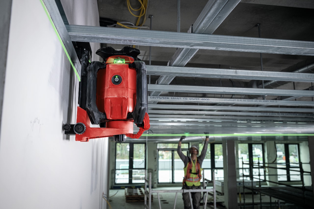 Hilti rotating laser is attached to a wall and construction worker working in the background.