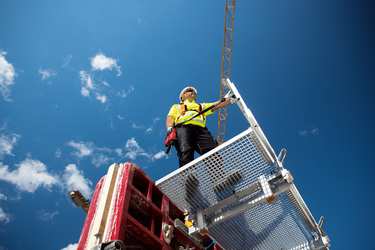 Man in yellow vest standing on a platform below blue sky. 