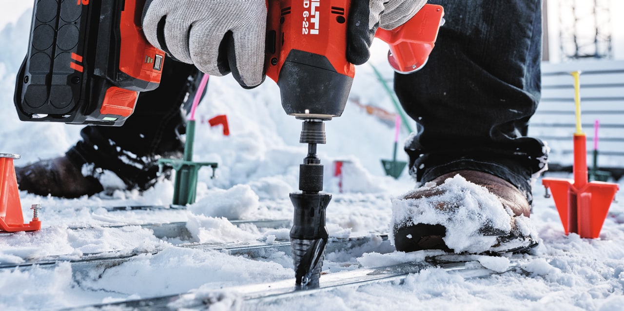 man using impact driver on snowy ground