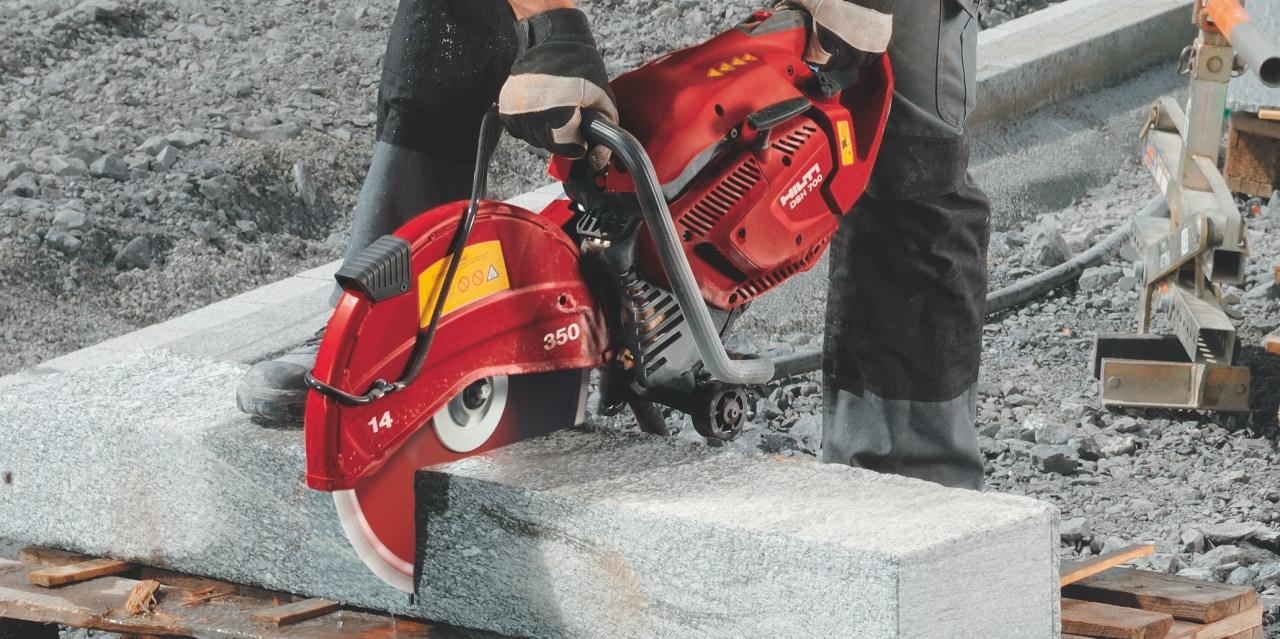 Man using red Hilti cut- off saw to cut concrete block. 
