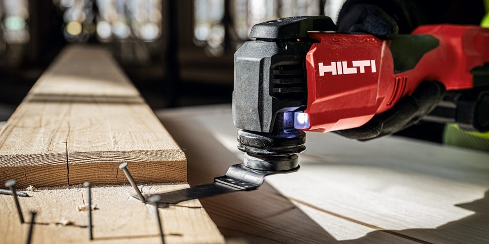 Man using red Hilti Multi tool to cut off nails from timber. 